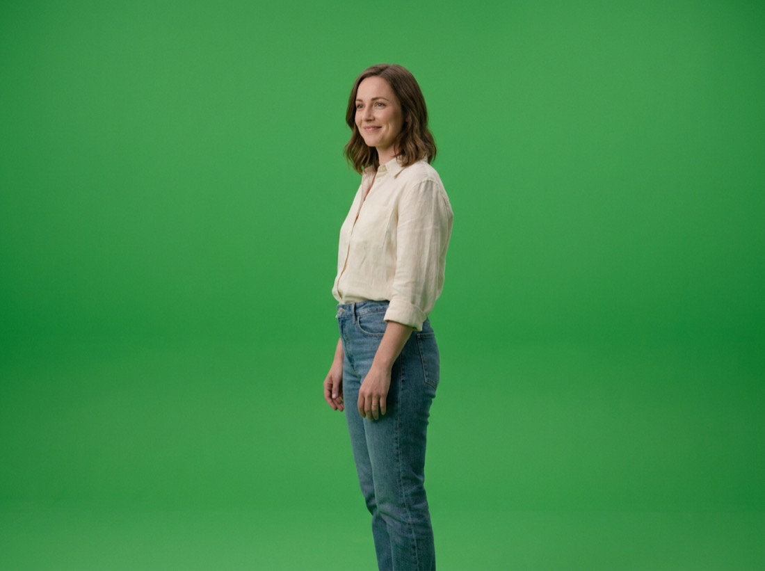 A woman standing in front of a plain green screen backdrop, as the video was filmed.